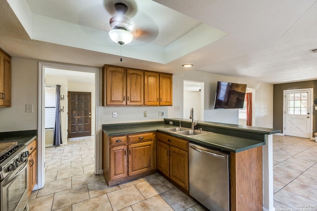 kitchen featuring dark countertops, appliances with stainless steel finishes, brown cabinets, a peninsula, and a tray ceiling