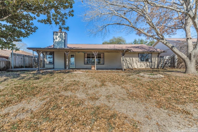 rear view of house with covered porch, a chimney, fence, and a lawn