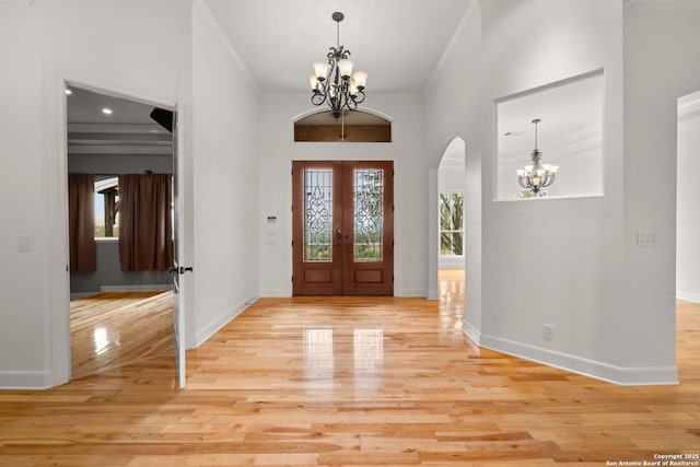 entrance foyer featuring ornamental molding, french doors, light wood-style floors, and a notable chandelier