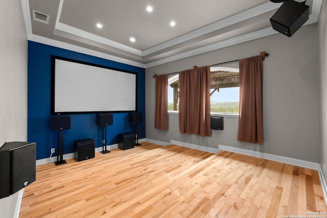 cinema featuring light wood finished floors, ornamental molding, a raised ceiling, and visible vents