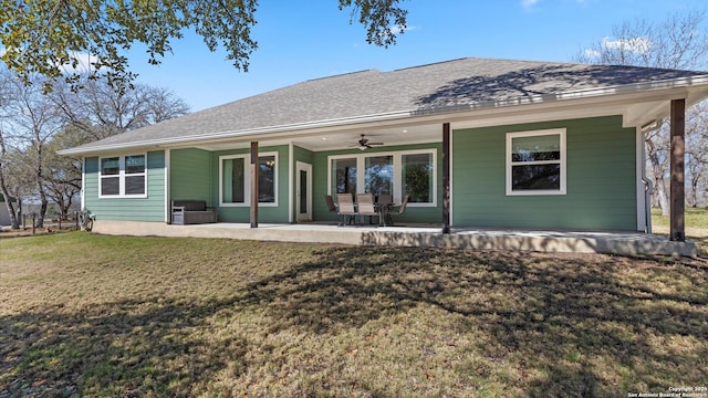 rear view of house with ceiling fan, roof with shingles, a lawn, and a patio