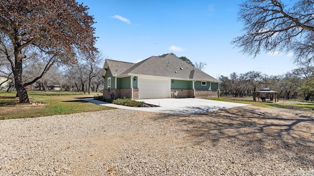 view of side of property featuring concrete driveway, brick siding, an attached garage, and a gazebo