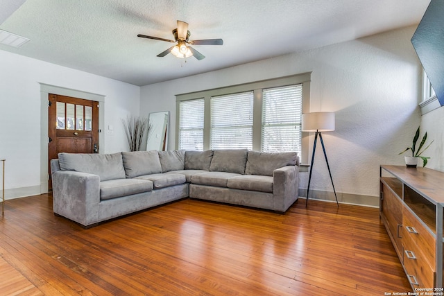 living room featuring a textured ceiling, dark wood-style flooring, visible vents, a ceiling fan, and baseboards