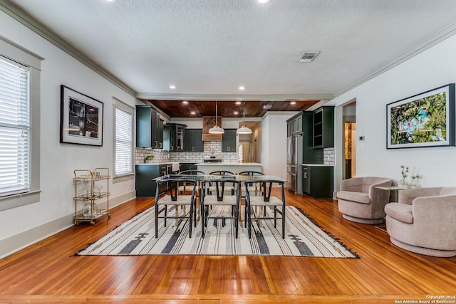 dining area with a textured ceiling, hardwood / wood-style floors, visible vents, and crown molding