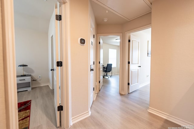 hallway with light wood finished floors, attic access, and baseboards