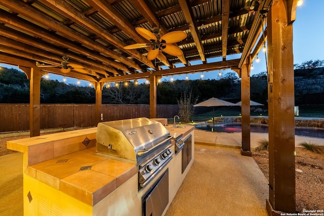 view of patio with an outdoor pool, a fenced backyard, a grill, and an outdoor kitchen