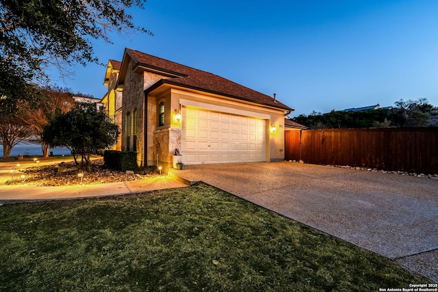 property exterior at dusk featuring an attached garage, stone siding, fence, and concrete driveway