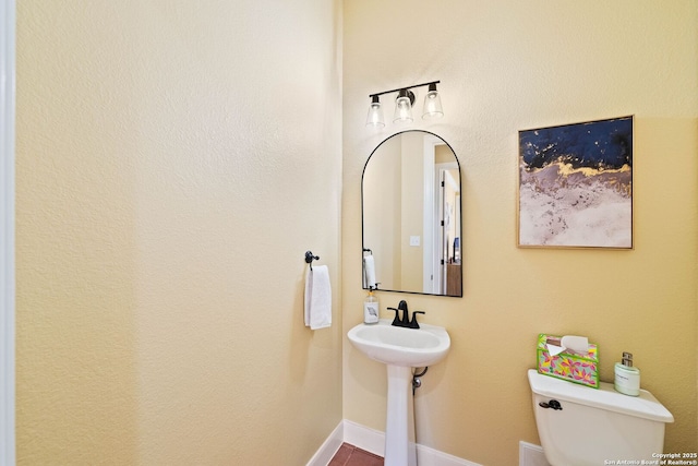 half bathroom featuring a sink, toilet, and baseboards