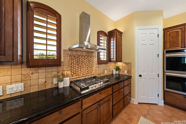 kitchen featuring wall chimney range hood, plenty of natural light, light tile patterned floors, and appliances with stainless steel finishes