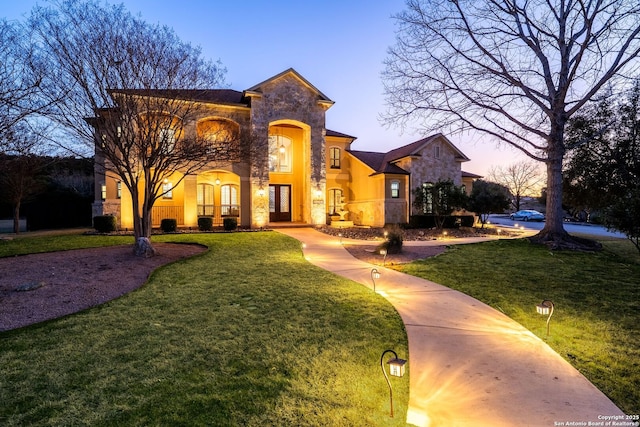 view of front of house featuring stone siding, a lawn, and stucco siding