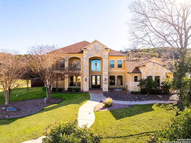 mediterranean / spanish home with stone siding, stucco siding, a front lawn, and french doors