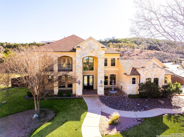 view of front of house with french doors, roof with shingles, stucco siding, a front yard, and stone siding