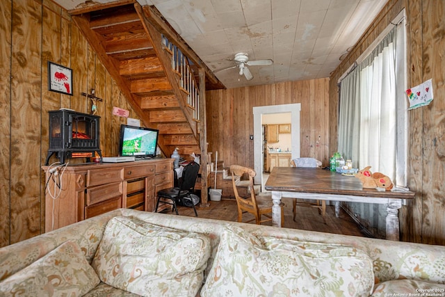 living room with stairway, ceiling fan, and wooden walls