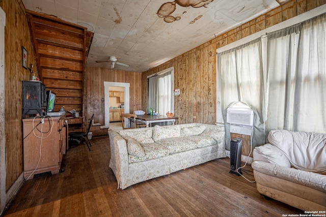 living area with a ceiling fan, wood-type flooring, and wooden walls