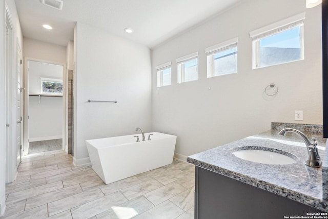 bathroom featuring a sink, visible vents, a soaking tub, double vanity, and a walk in closet