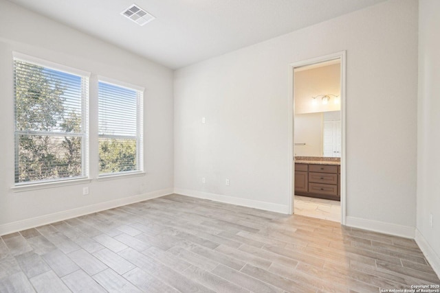 unfurnished bedroom with ensuite bath, light wood-style floors, baseboards, and visible vents