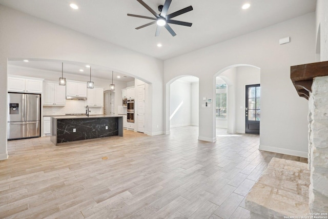 unfurnished living room featuring arched walkways, recessed lighting, ceiling fan, light wood-type flooring, and baseboards