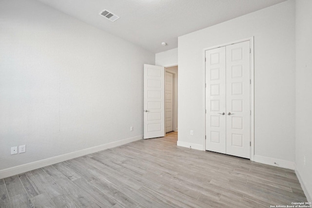 unfurnished bedroom with light wood-style floors, a closet, visible vents, and baseboards