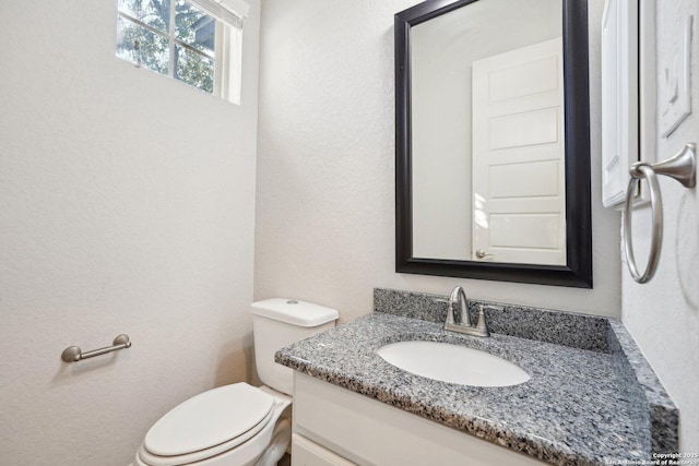 half bath featuring toilet, a textured wall, and vanity