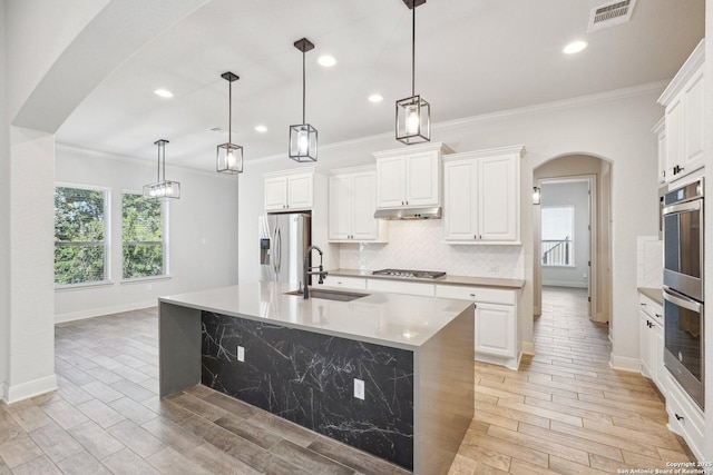 kitchen with arched walkways, stainless steel appliances, light countertops, visible vents, and a kitchen island with sink