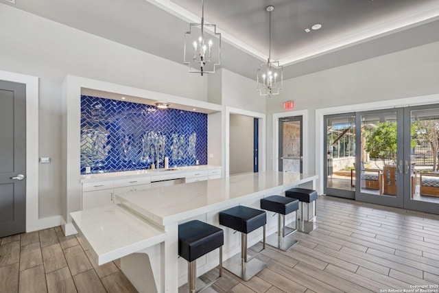 kitchen featuring light stone counters, a breakfast bar, decorative light fixtures, wood finish floors, and white cabinetry