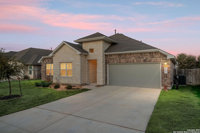 view of front facade featuring concrete driveway, a yard, an attached garage, and central air condition unit