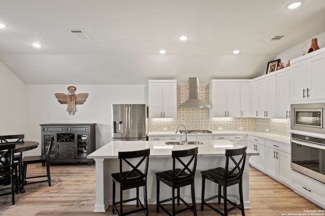 kitchen featuring wall chimney range hood, a center island with sink, appliances with stainless steel finishes, and light countertops