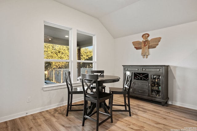 dining room featuring baseboards, vaulted ceiling, and light wood finished floors