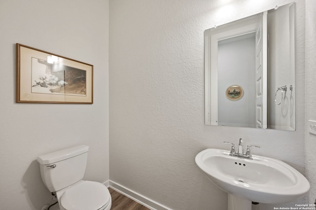 bathroom with baseboards, a textured wall, toilet, wood finished floors, and a sink