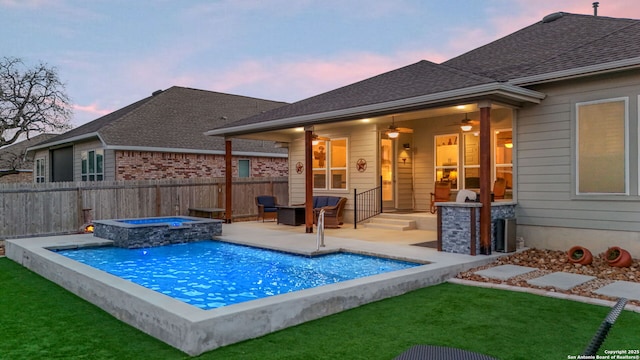 pool at dusk with a fenced in pool, a yard, a ceiling fan, fence, and an in ground hot tub