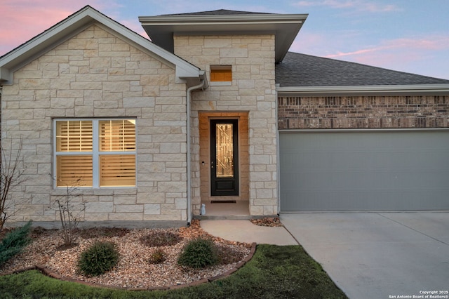 view of front of property featuring a garage, stone siding, driveway, and a shingled roof