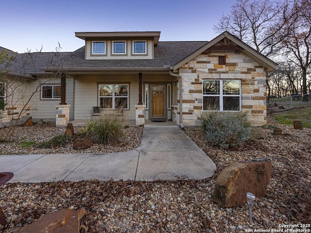 view of front facade with stone siding and a shingled roof