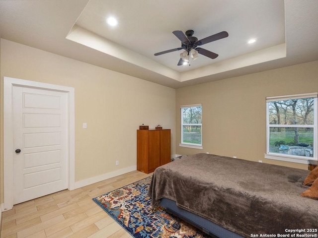 bedroom with light wood-style flooring, a tray ceiling, baseboards, and recessed lighting