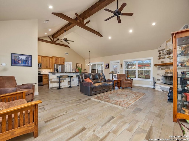 living area featuring light wood finished floors, visible vents, beamed ceiling, a stone fireplace, and high vaulted ceiling