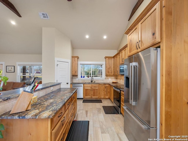 kitchen with stainless steel appliances, a sink, visible vents, vaulted ceiling, and dark stone countertops