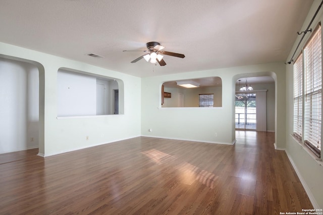 spare room featuring arched walkways, visible vents, wood finished floors, baseboards, and ceiling fan with notable chandelier