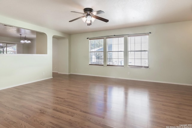 empty room with baseboards, arched walkways, wood finished floors, and ceiling fan with notable chandelier