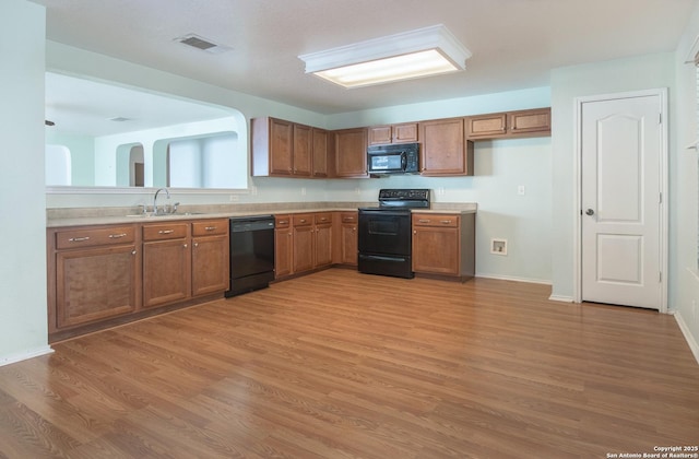 kitchen featuring brown cabinets, light countertops, visible vents, a sink, and black appliances