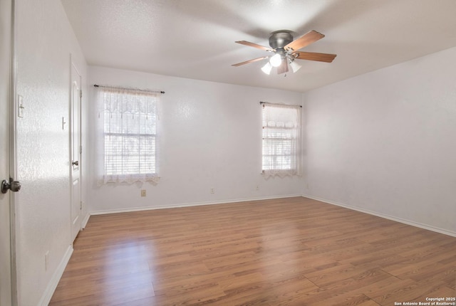 spare room featuring baseboards, a healthy amount of sunlight, a ceiling fan, and light wood-style floors