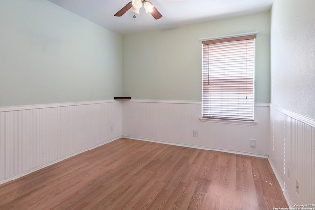 empty room featuring a wealth of natural light, a wainscoted wall, ceiling fan, and wood finished floors