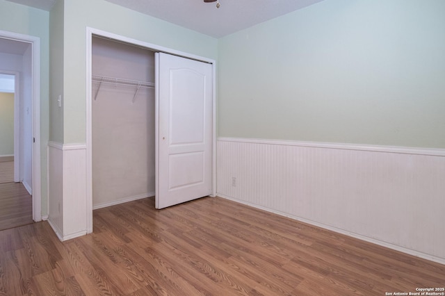 unfurnished bedroom with a closet, wainscoting, and wood finished floors