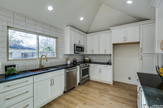 kitchen with white cabinets, dark countertops, lofted ceiling, stainless steel appliances, and a sink