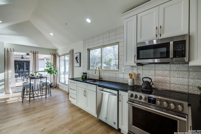 kitchen with dark countertops, appliances with stainless steel finishes, vaulted ceiling, white cabinetry, and a sink