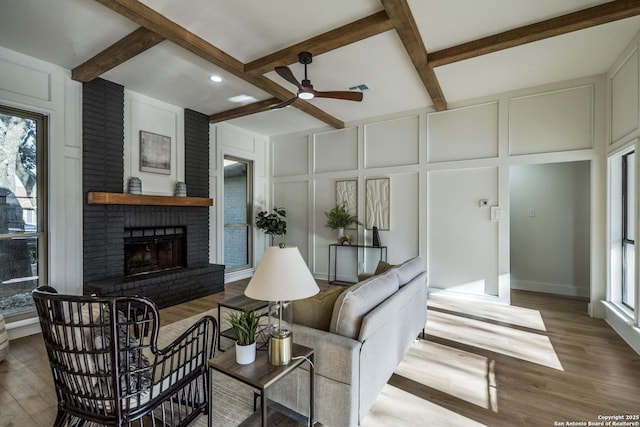 living room featuring visible vents, wood finished floors, a brick fireplace, a decorative wall, and beam ceiling