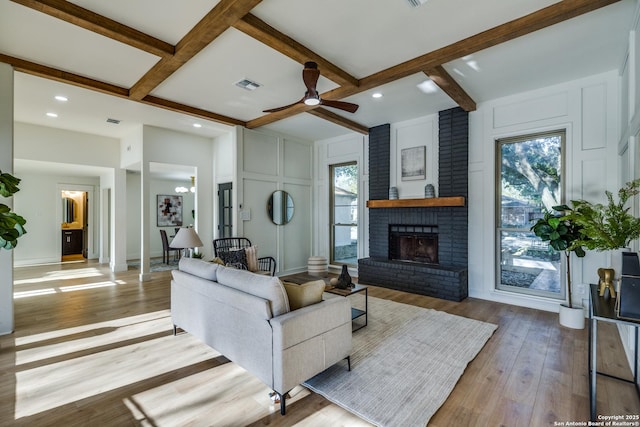 living room featuring beam ceiling, visible vents, a decorative wall, light wood-style floors, and a brick fireplace