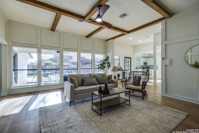 living room with ceiling fan, light wood finished floors, visible vents, and a decorative wall