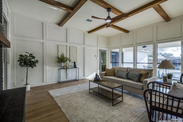 living room with beam ceiling, visible vents, a decorative wall, ceiling fan, and wood finished floors