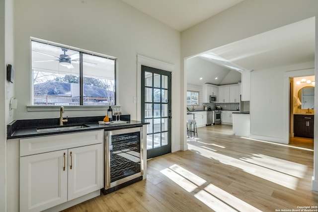 kitchen featuring wine cooler, a sink, white cabinetry, vaulted ceiling, and appliances with stainless steel finishes