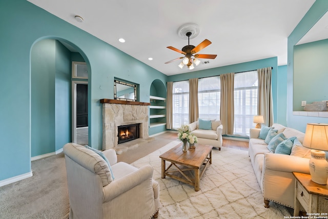 living area with light carpet, baseboards, built in features, ceiling fan, and a fireplace