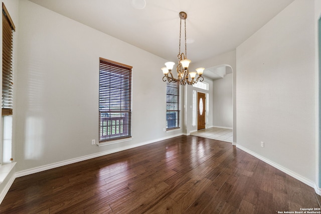 empty room with a notable chandelier, baseboards, arched walkways, and wood finished floors